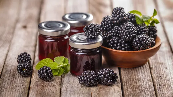 Frische Brombeeren und Gläser mit Brombeermarmelade.