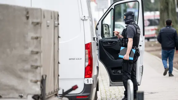 Ein Polizist steht an einem Transporter vor der Wohnung der ehemaligen RAF-Terroristin Daniela Klette.
