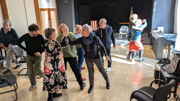Eine Gruppe an Seniorinnen und Senioren tanzt durch einen Theatersaal.