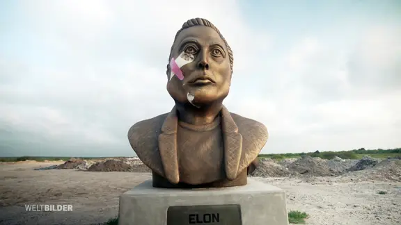 Eine Statue des Musk Kopfes in der Wildnis, im Gesicht ein weiß-pinkes X.