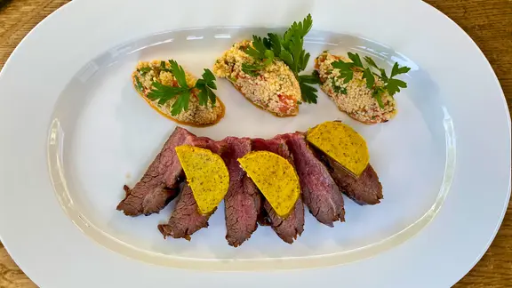 Flanksteak vom Grill mit Currybutter und Melonen-Taboulé auf einem Teller angerichtet.