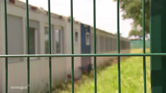Hinter einem Zaun stehen Wohncontainer.