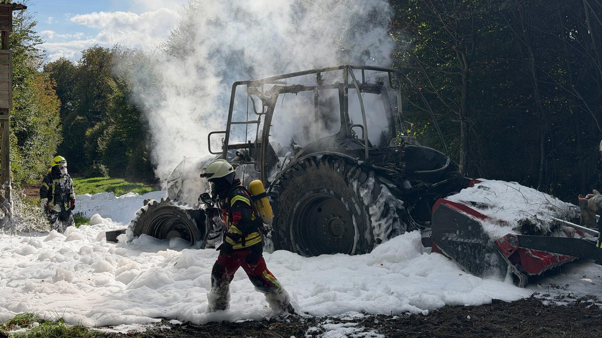 Zwei Feuerwehrleute mit Atemschutz stehen vor dem ausgebrannten, qualmenden Traktor. | Christopher Sakel, Fachzug Bevölkerungswarnung Landkreises Northeim
