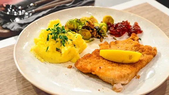 Putenschnitzel "Wiener Art" mit Kartoffel-Steckrüben-Stampf und Kohlsprossen auf einem Teller angerichtet.
