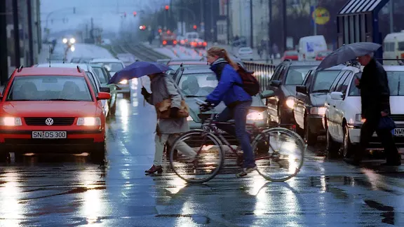 Bei Regen passieren Fußgänger und Fahrradfahrer eine Kreuzung in Schwerin.