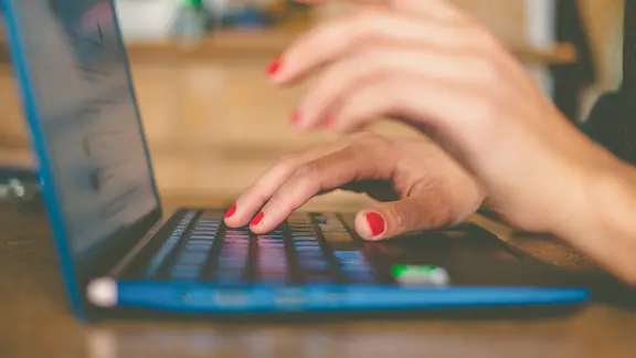 Hände mit lackierten Fingernägeln tippen auf einem Laptop herum.
