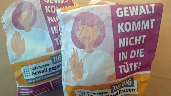 Zwei Papiertüten mit dem Schriftzug "Gewalt kommt nicht in die Tüte!" stehen auf einem Tisch.