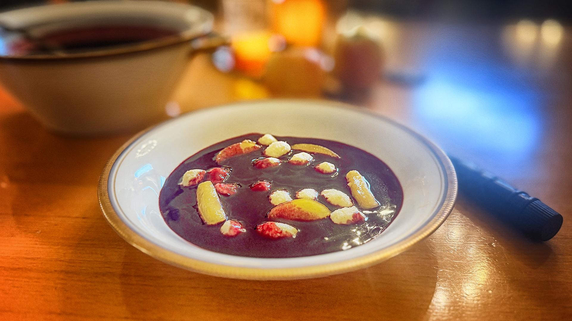 Fliederbeersüppchen mit Apfel und Grießklößchen auf einem weißen Teller serviert | NDR