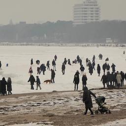 Menschen gehen am Ufer der zugefrorenen Ostsee spazieren