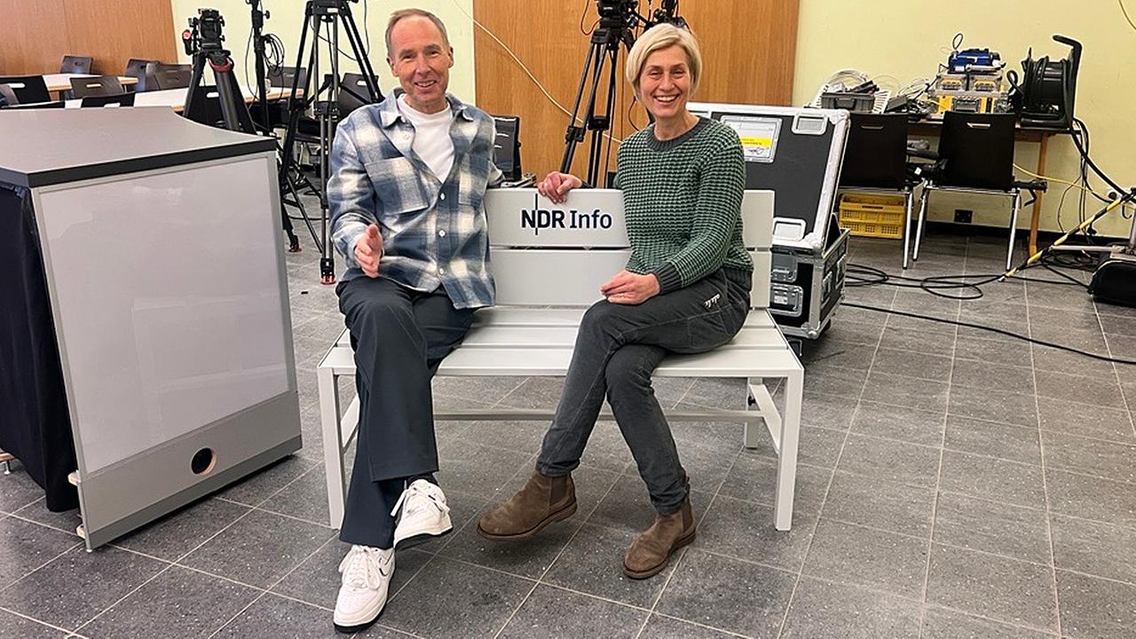 Die Moderatoren Stefan Schlag und Susanne Stichler sitzen auf einer Bank.