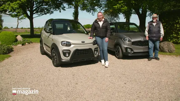 Eine junge Frau und ein älterer Mann stehen neben ihrem Microcar.