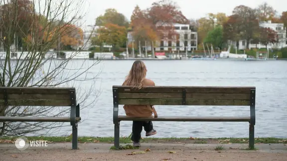 Eine Frau sitzt allein auf einer Bank. | Screenshot Eine Frau sitzt allein auf einer Bank.