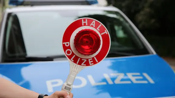 Ein Polizist hält eine Polizeikelle vor einem Streifenwagen.