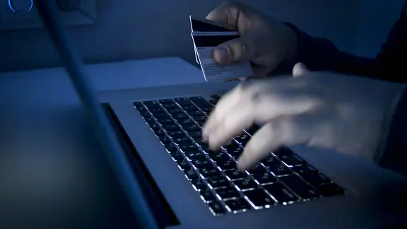 Ein Krimineller sitzt am Computer und hat EC-Karten in der Hand.
