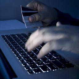 Ein Krimineller sitzt am Computer und hat EC-Karten in der Hand.