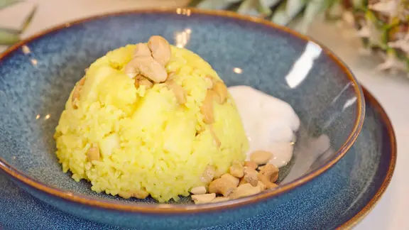 Eine Schale mit einem gelben Reis, garniert mit Cashewkernen. 