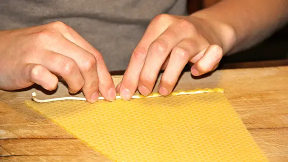 Für eine Kerze, die sich nach oben spiralförmig verjüngt, schneidet man Bienenwachsplatten dreieckig zu. | MIRELLA PAPPALARDO, MIRELLA PAPPALARDO Szene der eigenhändigen Herstellung von Kerzen.