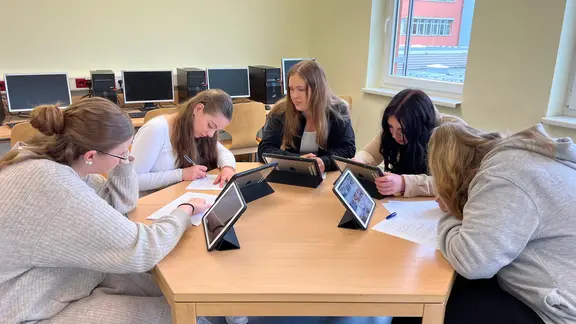 Schülerinnen sitzen um einen Tisch mit iPads in den Händen in einem Klassenraum der KSG Bad Bevensen in der Hand.