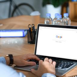 Ein Mann sitzt mit aufgesetzten Kopfhörern vor einem Laptop, der die Website von Google zeigt