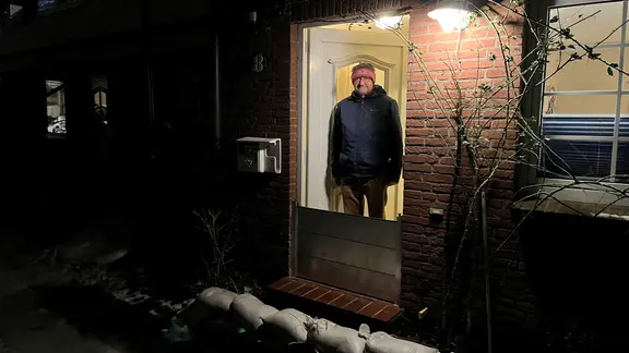 Jesper Nielsen wohnt seit 1987 im Hafengang - abgesehen vom großen Sturm im Oktober 2023 sei es dort ruhig gewesen. Jetzt beobachtet er das Hochwasser. | Moritz Mayer Ein Mann steht in der Haustür.