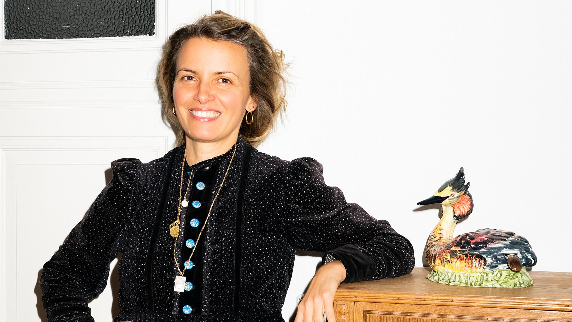 Eine Frau steht vor einer weißen Wand; neben ihr steht eine bunte Ente auf einem Schrank | Eray Aydin