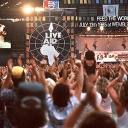 Jubelnde Zuschauer vor einer Bühne - auf einer Leinwand: der singende Freddy Mercury.