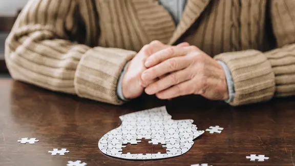 Ein älterer Mann sitzt vor einem Puzzle in kopfform