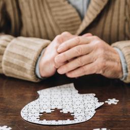 Ein älterer Mann sitzt vor einem Puzzle in kopfform