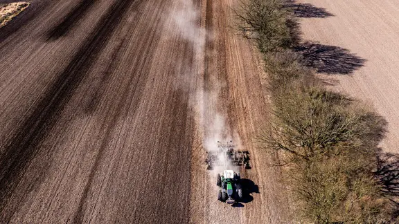 Luftaufnahme eines Traktors, der eine Egge über einen trockenen Acker zieht, um ihn für die Aussaat vorzubereiten.