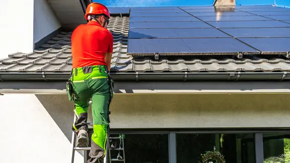 Ein Techniker bei der Installation von Solarzellen auf dem Dach eines Hauses.