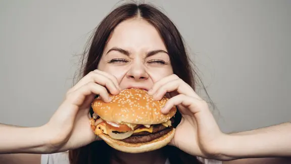 Eine Frau beißt in einen Burger. | Picture Alliance, picture alliance / Bildagentur-online/Blend Images | Blend Images/Dmitry Ageev Eine Frau beißt in einen Burger.