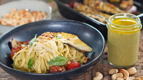 Ein dunkler Teller mit Linguine, Auberginen-Pesto, Ofentomaten und -aubergine sowie Basilikumblättern