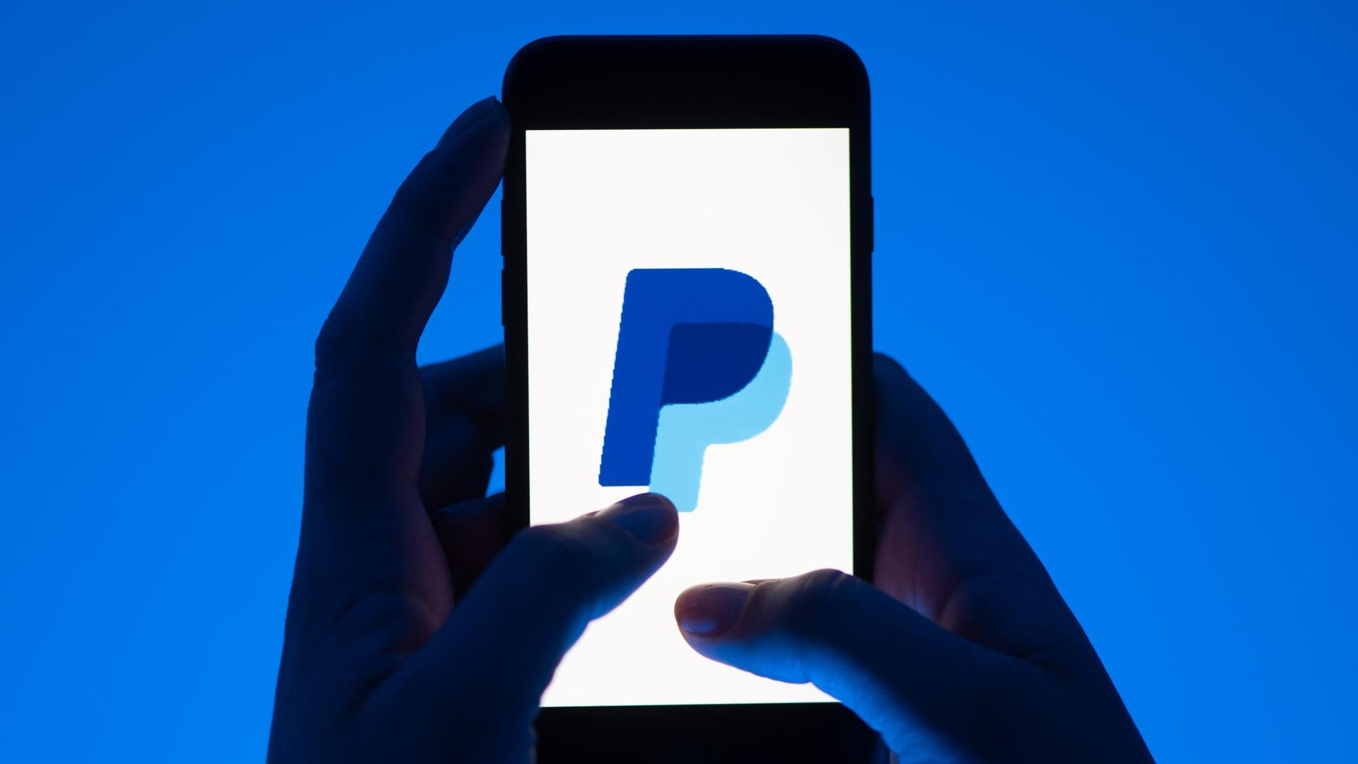 Eine Hand hält ein Smartphone mit dem Logo des Bezahldienstes Paypal. | Sebastian Kahnert/dpa