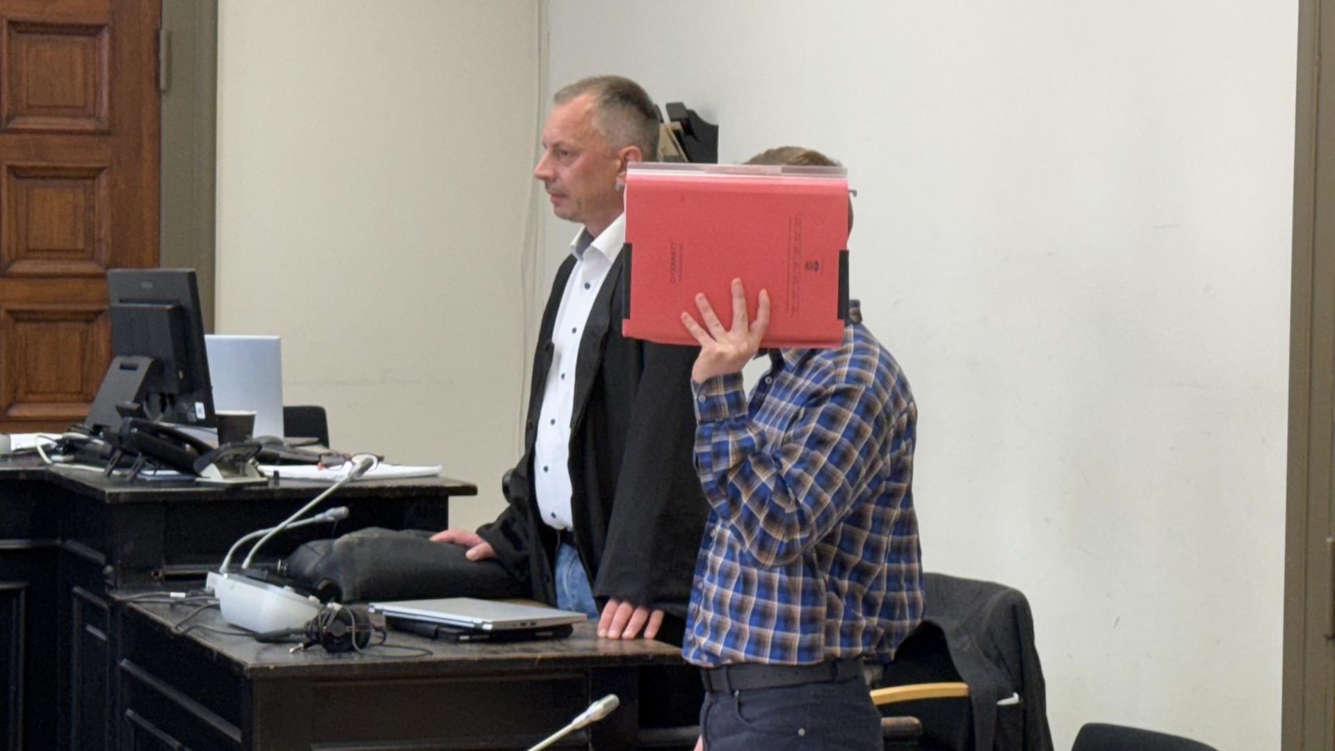 Ein Angeklagter hält sich einen Aktenordner im Gerichtssaal vor das Gesicht. | NDR