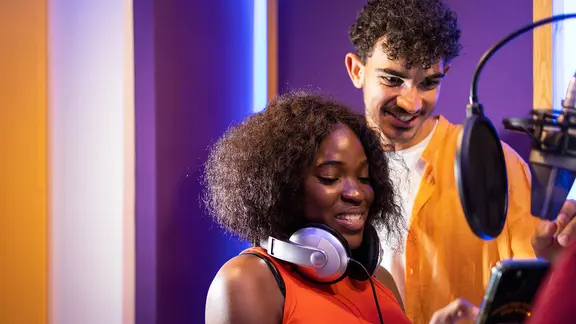 Eine Frau und ein Mann mit Kopfhörern und Smartphone in einem Studio (Symbolfoto).