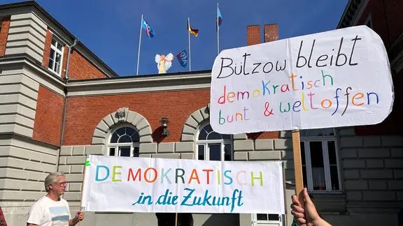 Mehrere Menschen demonstrieren gegen die AfD-Flaggen auf dem Bützower Bahnhof