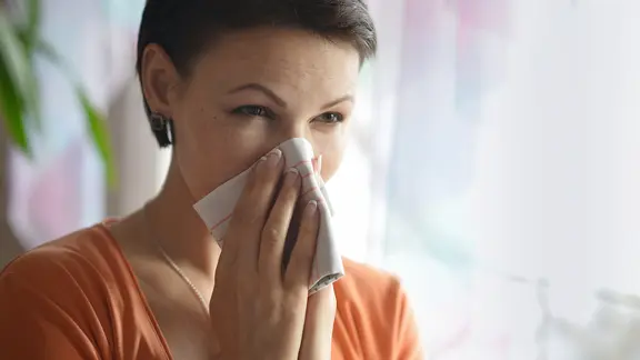 Frau schnupft in ein Taschentuch.