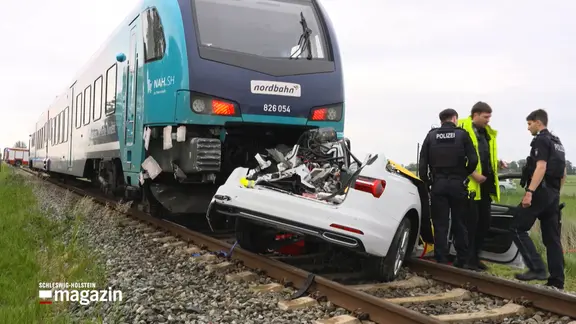 Rettungskräfte stehen vor einem Zug vor dem ein Pkw steht
