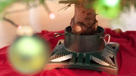 Nahaufnahme eines Weihnachtsbaumständers, in dem der Stamm einer geschmückten Tanne steht.