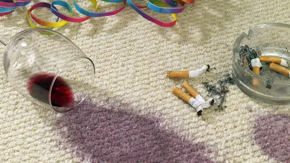 Auf einem Teppich liegen ein ausgekipptes Glas Rotwein und Zigarettenkippen