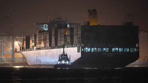 Ein großer MSC-Frachter im Dunkeln, davor ein Schlepper.