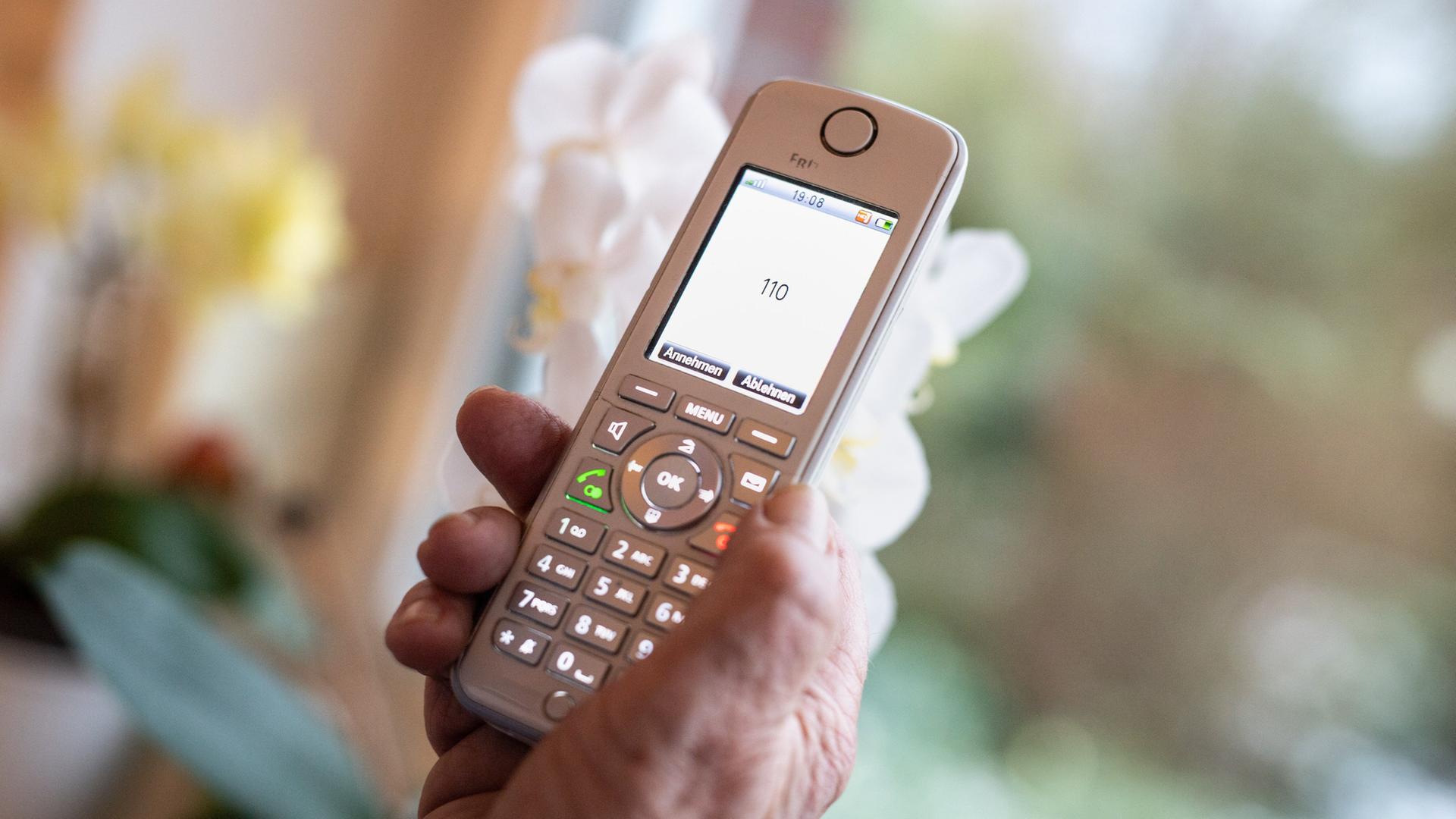 Eine alte Dame hält ein Telefon in ihren Händen, auf dem ein Anruf von der Notrufnummer 110 zu kommen scheint | picture alliance / Matthias Balk