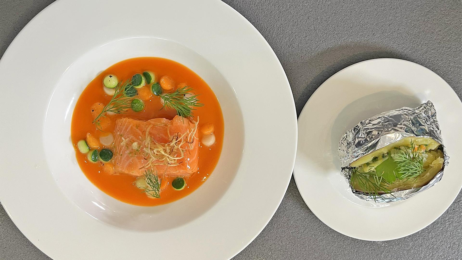 Lachs-Würfel mit Karottenjus auf einem weißen Teller, daneben Ofenkartoffel mit Gewürzbutter | NDR