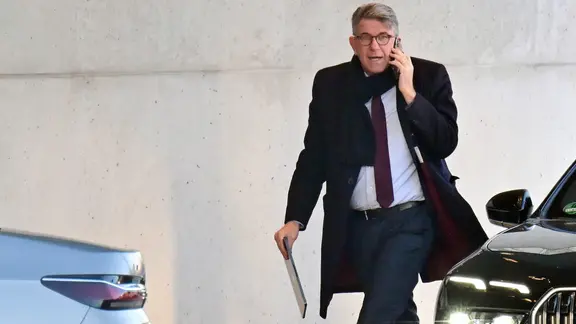 Ο Wolfram Weimer περνάει δίπλα από δύο αυτοκίνητα, ένα κινητό στο αυτί του και ένα tablet στο χέρι. | Sebastian Gollnow/dpa +++ dpa-Bildfunk +++ Ο Wolfram Weimer περνάει δίπλα από δύο αυτοκίνητα, ένα κινητό στο αυτί του και ένα tablet στο χέρι.