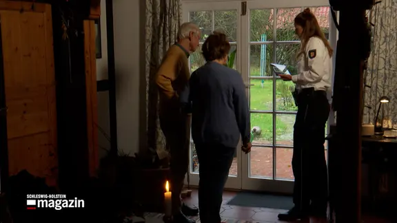 Eine Polizistin im Gespräch mit zwei Personen in einem Haus