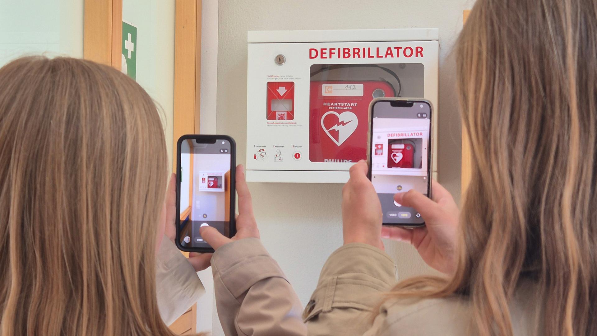 Zwei Schülerinnen fotografieren mit ihren Smartphones einen Defibrillator. | NDR, Britta Nareyka
