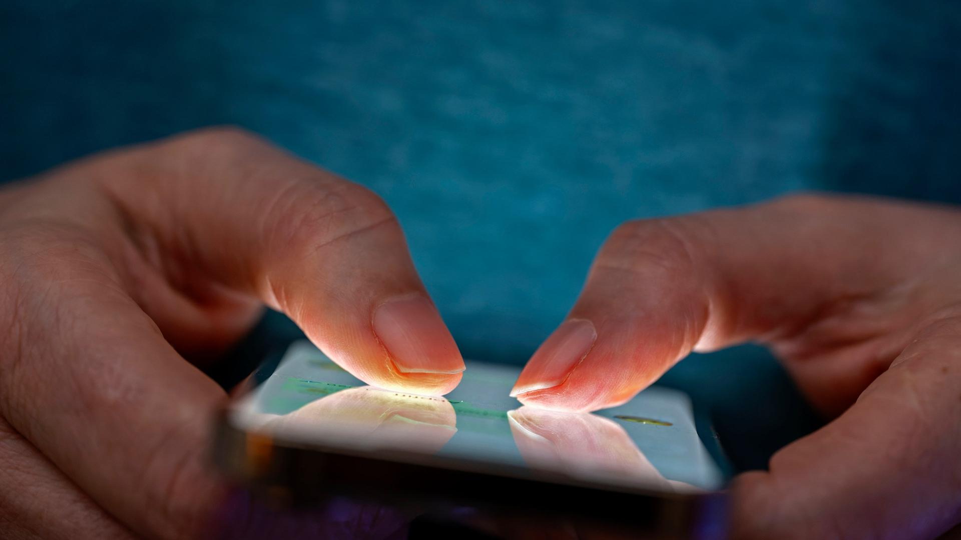Das Bild zeigt eine Person, die in einer schlecht beleuchteten Umgebung ein Smartphone benutzt. | picture alliance / M.i.S. | Bernd Feil