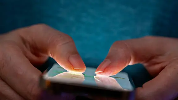 Das Bild zeigt eine Person, die in einer schlecht beleuchteten Umgebung ein Smartphone benutzt.