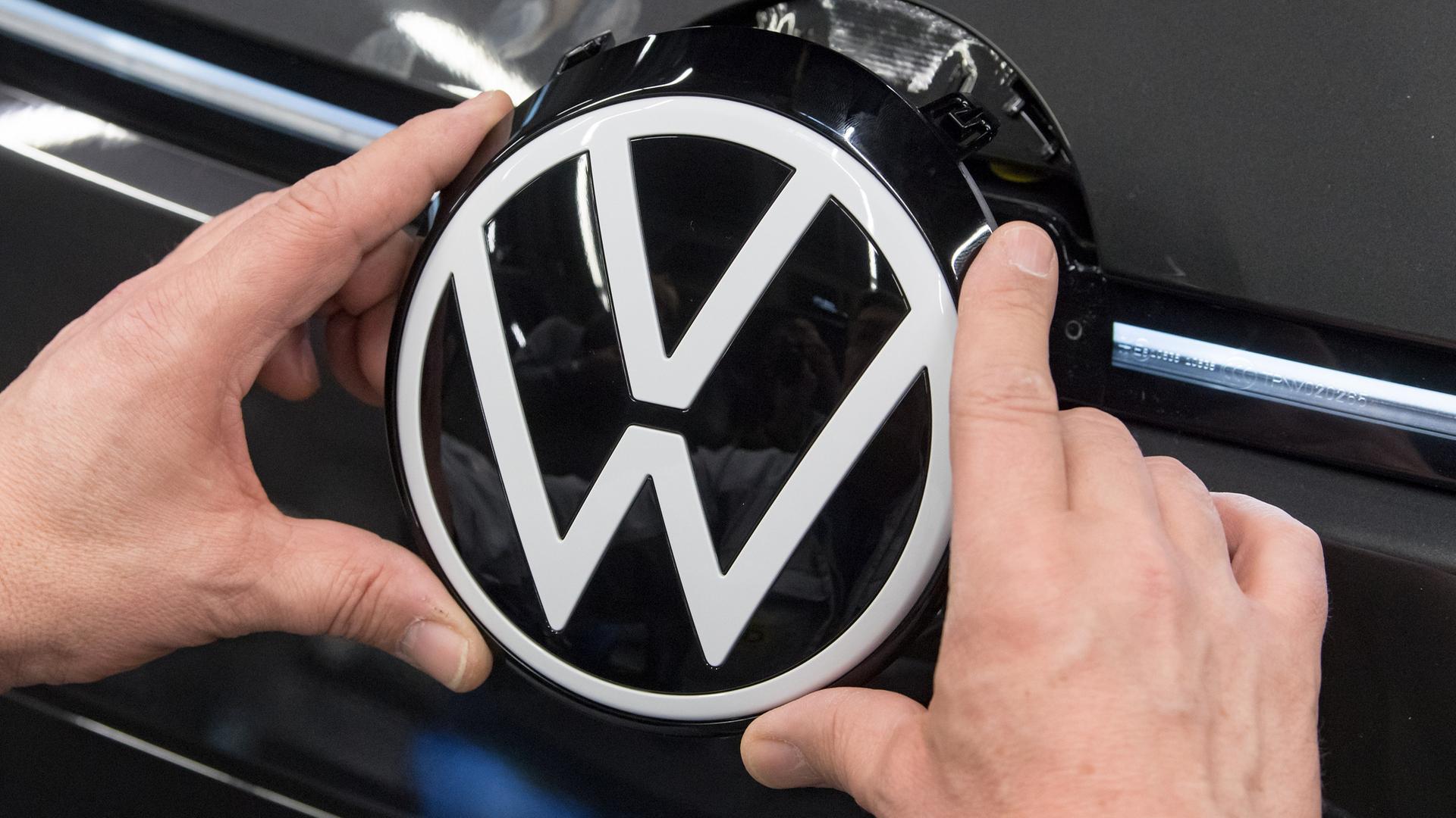 Ein Mitarbeiter von Volkswagen das VW-Logo in die Front eines Autos ein. | picture alliance/dpa, Hendrik Schmidt