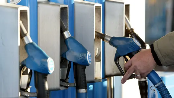 Ein Mann greift nach einer Zapfpistole an einer Tankstelle.